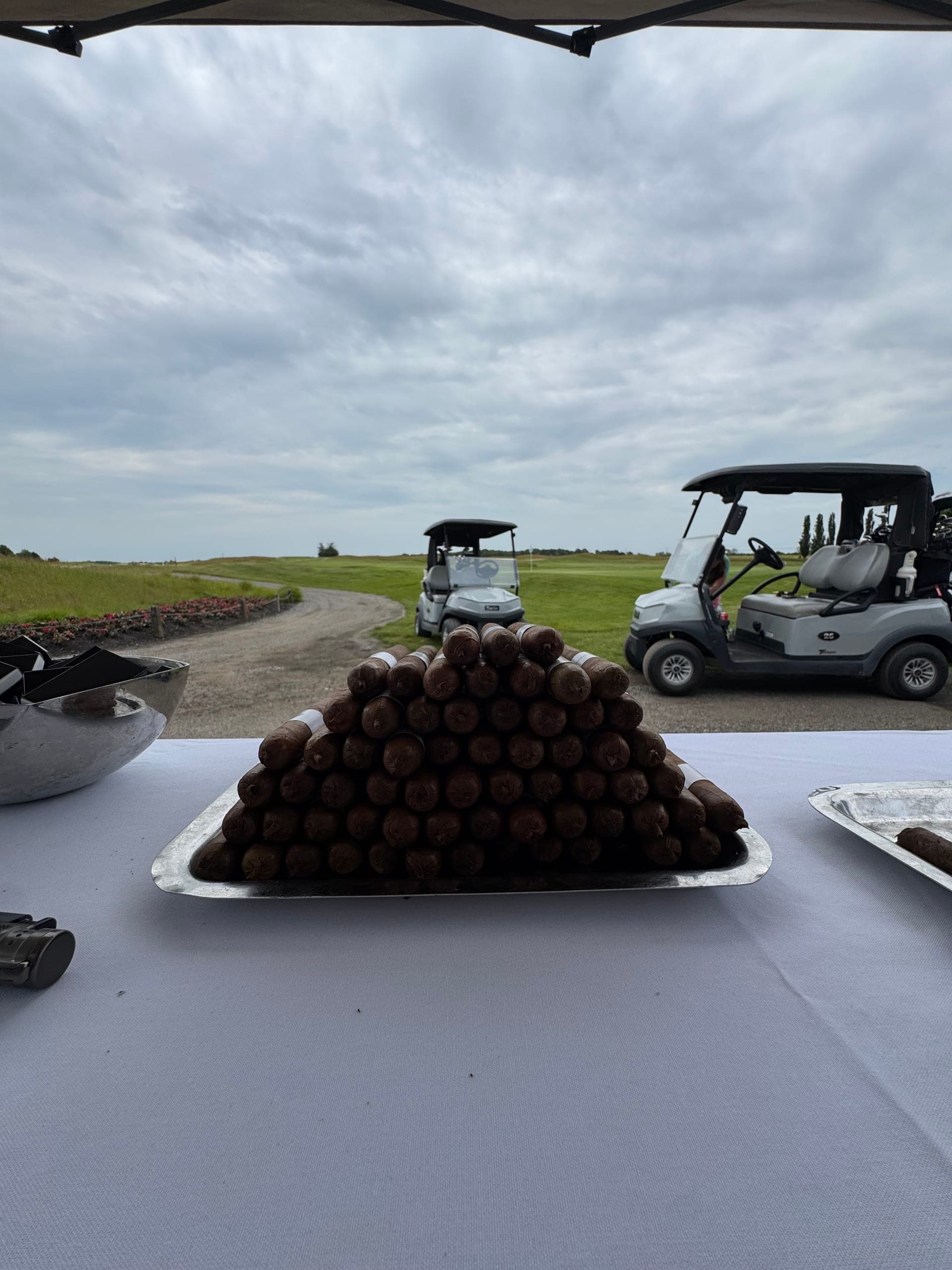 A pyramid of hand-rolled cigars on a tray overlooking a golf course with carts nearby