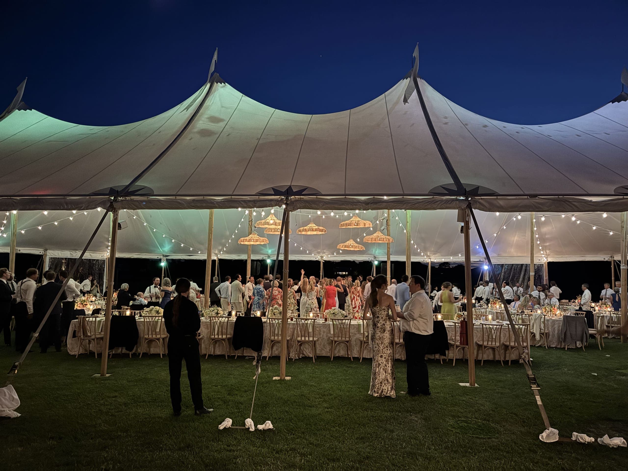 A couple dancing under a tented wedding reception lit with string lights
