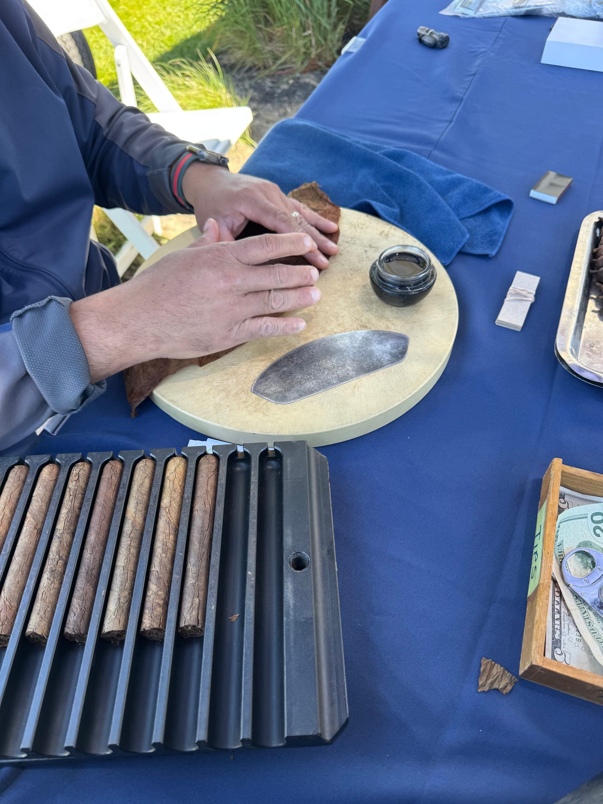 Hands rolling a cigar on a rolling board beside a cigar press